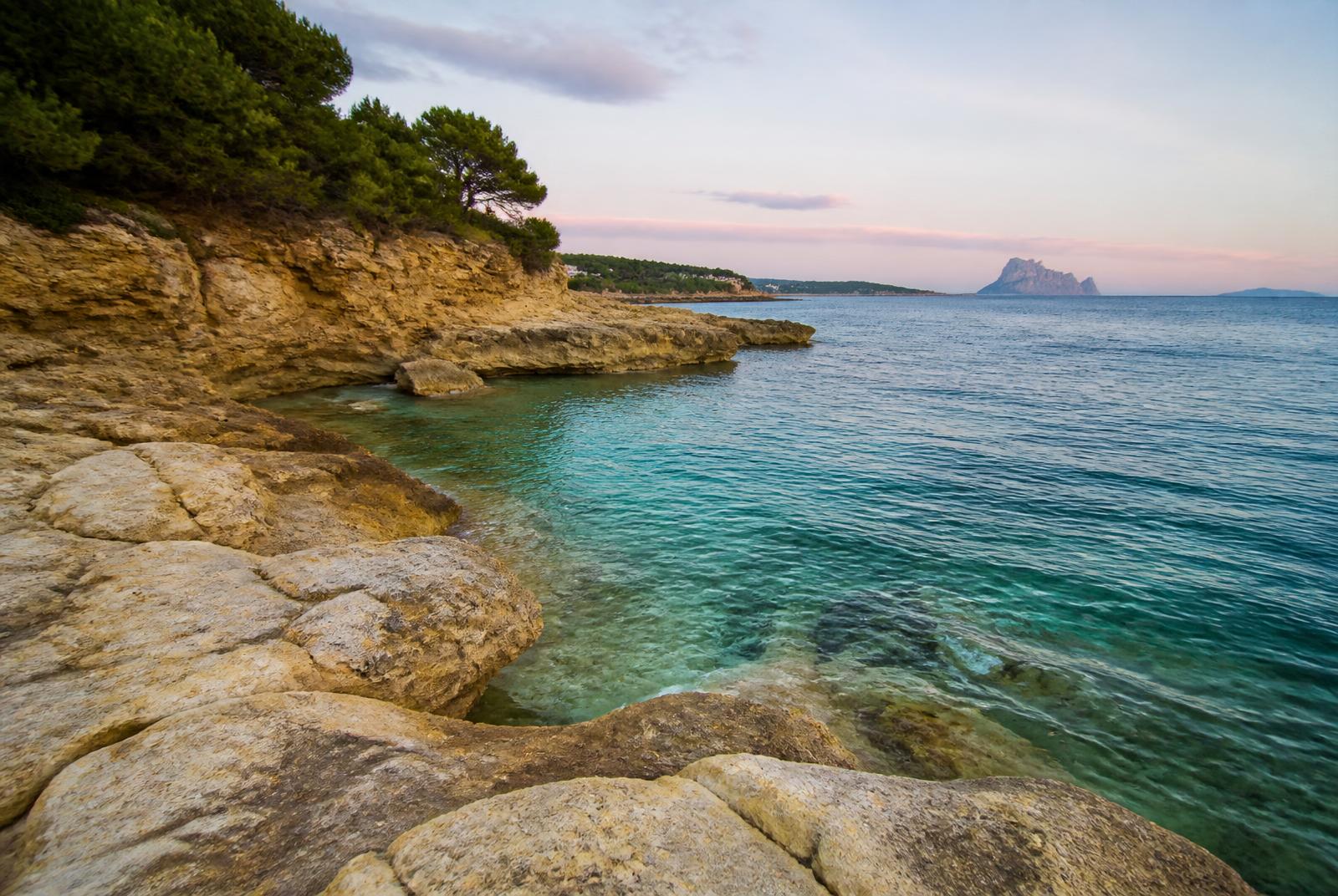 Cala Baladrar en Benissa Costa: agua turquesa transparente, acantilados de piedra ocre y pinos mediterráneos al amanecer